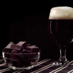 Cerveja com chocolate: uma combinação perfeita. Na imagem, pedaços de chocolate ao lado de uma taça de cerveja preta