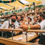 Curta o Dia da Cerveja Alemã como se estivesse na Oktberfest. Na imagem, um grupo de homens com trajes típicos está sentado em uma meda na Oktoberfest
