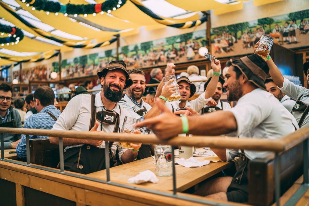 Curta o Dia da Cerveja Alemã como se estivesse na Oktberfest. Na imagem, um grupo de homens com trajes típicos está sentado em uma meda na Oktoberfest